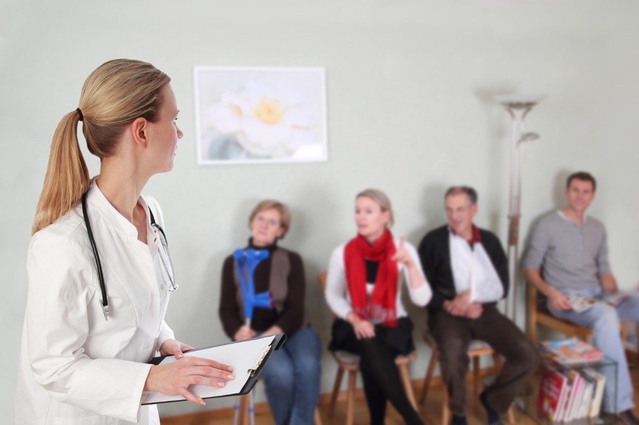 Ärztin steht vor ihren Patienten im Wartezimmer