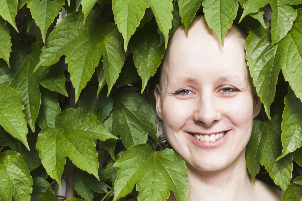 lächelnde Krebspatientin, von grünen Blättern umgeben