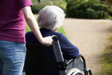 Junge Frau schiebt einen Rollstuhl, in dem eine alte Frau sitzt