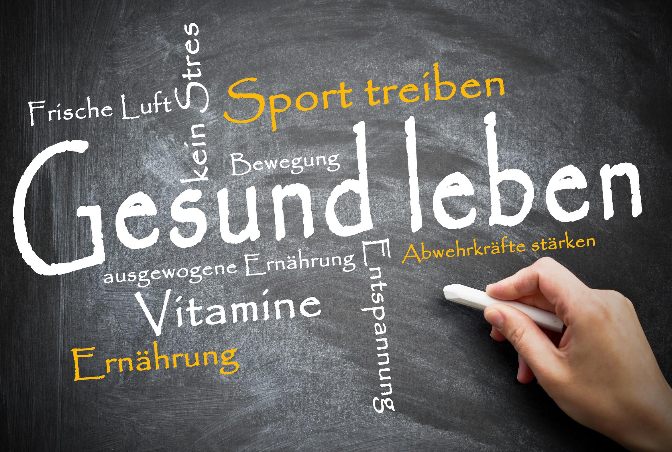 Eine Hand hat mit Kreide Begriffe wie Gesund leben, Sport treiben und Vitamine an eine Tafel geschrieben