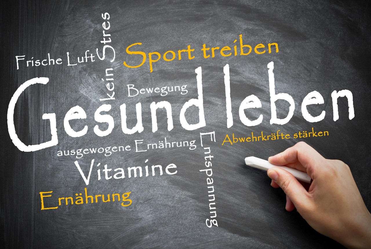 Eine Hand hat mit Kreide Begriffe wie Gesund leben, Sport treiben und Vitamine an eine Tafel geschrieben