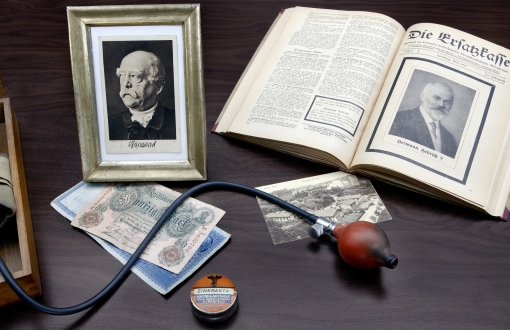 Foto zu 100 Jahre vdek: verschiedene Gegenstände wie ein Foto von Fürst Otto von Bismarck, die erste Verbandspublikation, Blutdruckmessgerät oder ein alter Fünfzig Mark Schein