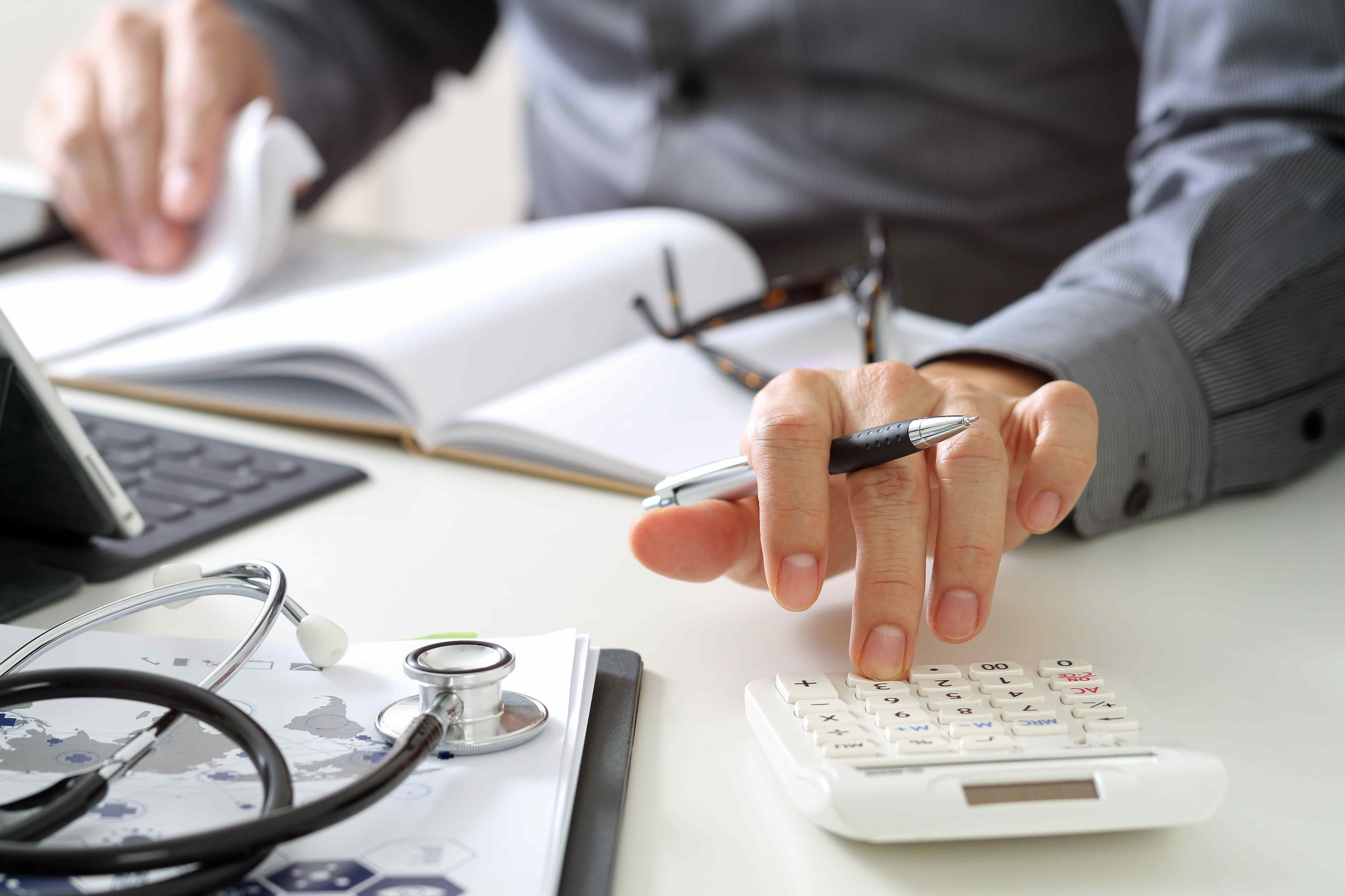 Mann am Schreibtisch sitzend Taschenrechner Krankenhausabrechnung Budget Finanzen Arztabrechnungen