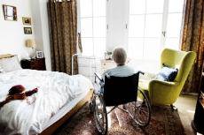 Seniorin sitzt in einem Rollstuhl in einem Zimmer und schaut aus dem Fenster