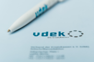 Ein Stift liegt auf der Rückseite eines Heftes, beide tragen das vdek-Logo