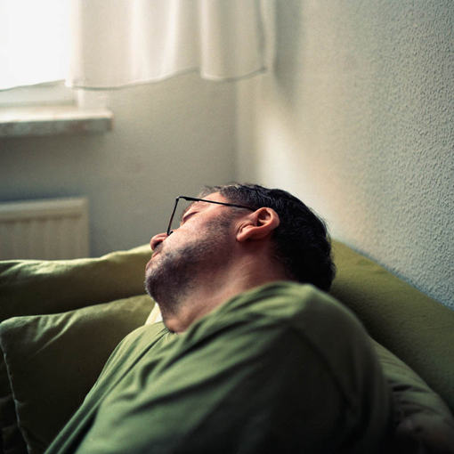 Portrait-Ansicht eines Mannes, der auf dem Wohnzimmersofa im Sitzen eingeschlafen ist.