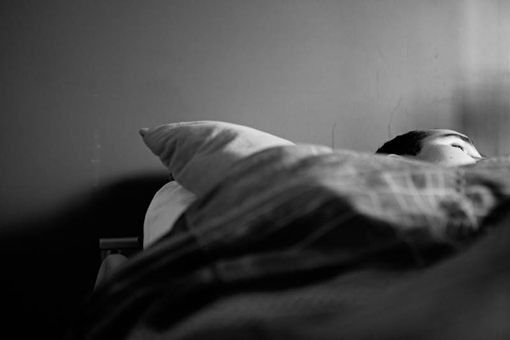 Blick auf ein Bett, eine weggeneigte Gesichtshälfte ist erkennbar.