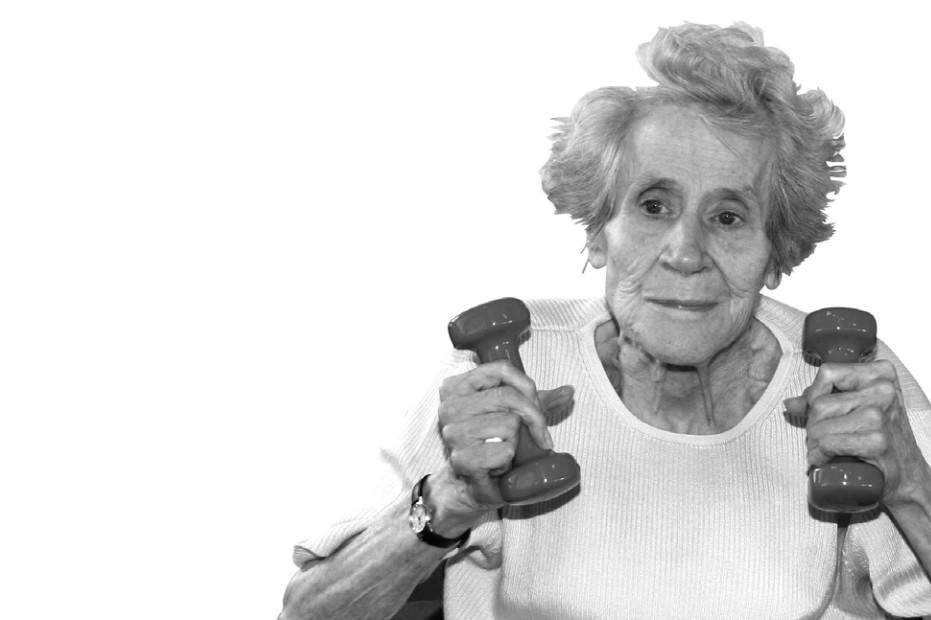 Portrait einer alten Frau in einem Stuhl, die mit zwei kleinen Hanteln trainiert.