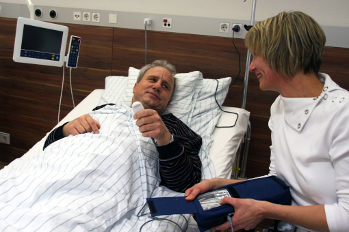Ein Mann liegt in einem Krankenbett, eine Krankenschwester sitzt neben ihm. 