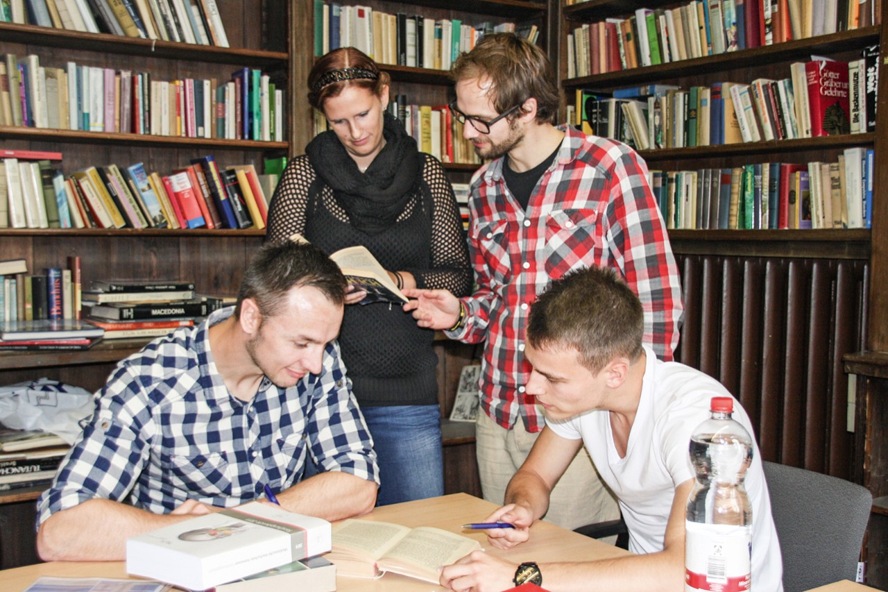 Junge Menschen lesen vor B&uuml;cherregalen
