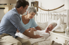 Arzt während des Hausbesuchs eines älteren Paares beim Gespräch am Krankenbett 
