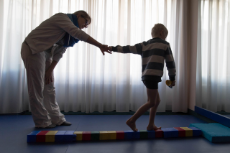 Eine Frau hält die Hand eines Jungen, der über einen Steg aus bunten Spiel-Bausteinen geht
