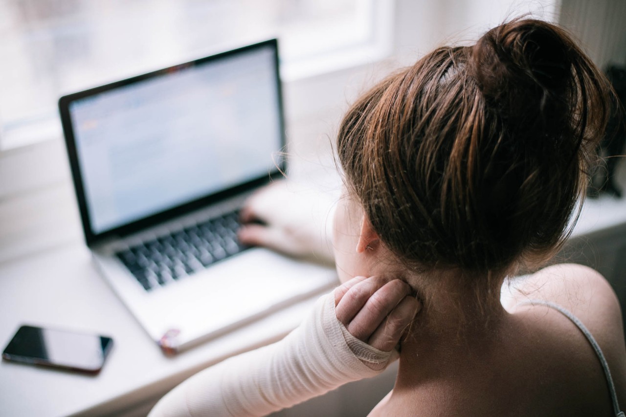 Junge Frau mit bandagierten Armen sitzt am Computer 