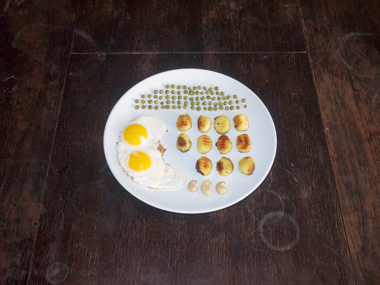 Auf einem Teller liegen systematisch angeordnet etliche Erbsen, elf Gnocchi, zwei Spiegeleier und drei Nüsse