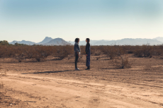 Zwei junge Frauen stehen sich in einer kargen Landschaft sehr nah gegenüber