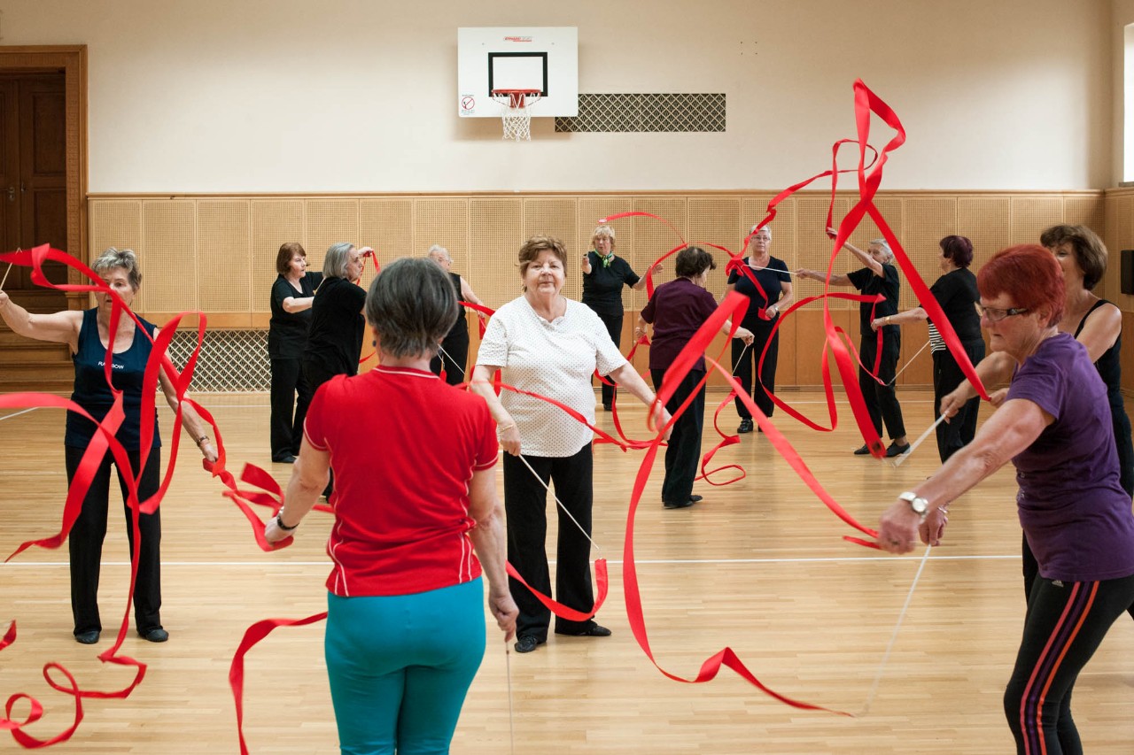Seniorinnen in einer Turnhalle machen Gymnastik mit roten Bändern aus der rhythmischen Sportgymnastik 