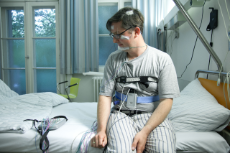 Frau sitzt mit Messgeräten und Sensoren am Körper auf einem Krankenbett