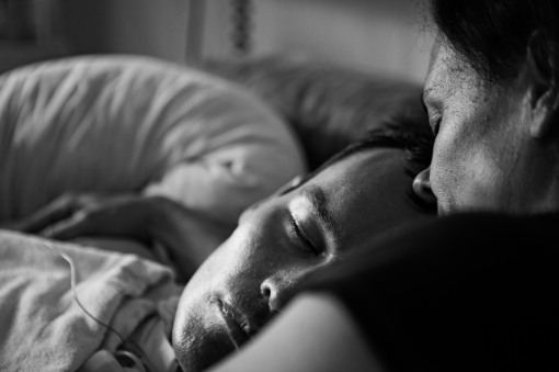 Portrait eines im Bett liegenden jungen Mannes, eine ältere Frau lehnt ihr Gesicht auf seine Stirn, beide mit geschlossenen Augen.