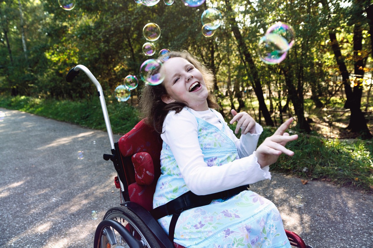 Fröhliche Frau im Rollstuhl in freier Natur, um sie herum Luftblasen.