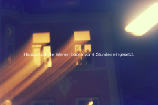 Zwei erleuchtete Hausfenster bei Nacht, davor die Aufschrift "Hausgeburt, die Wehen haben vor 4 Stunden eingesetzt."