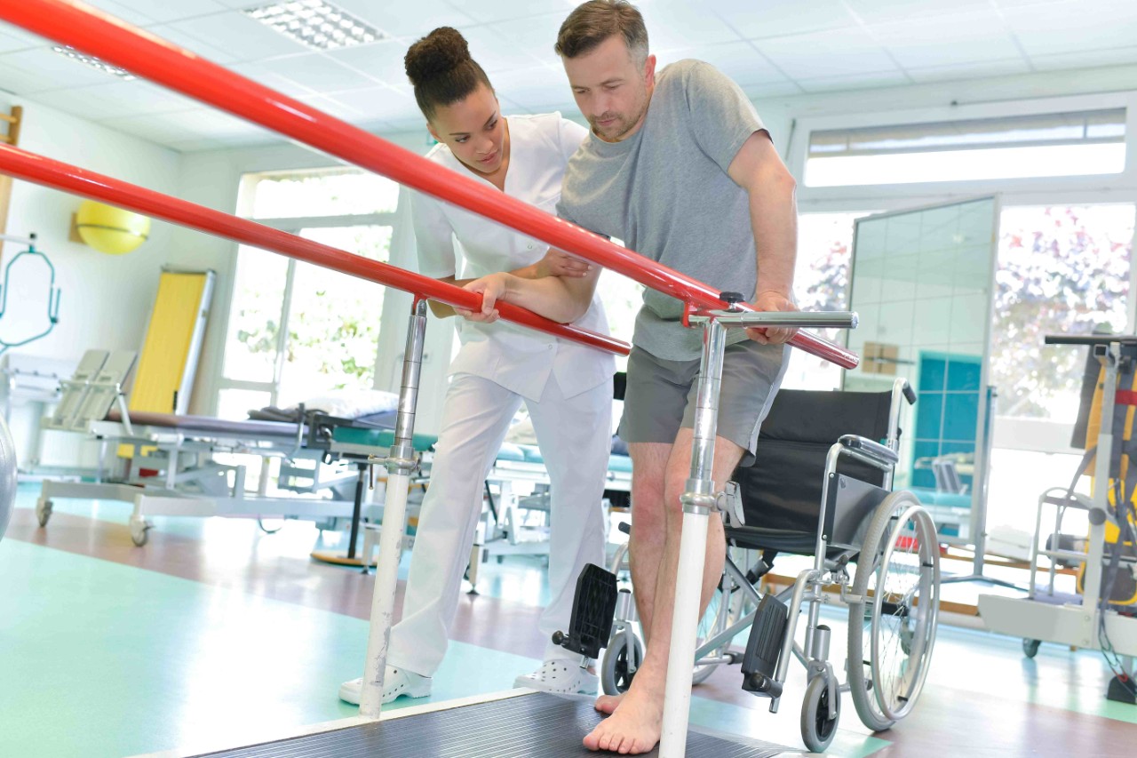 Krankengymnastik: Physiotherapeutin hilft Mann beim Gehen