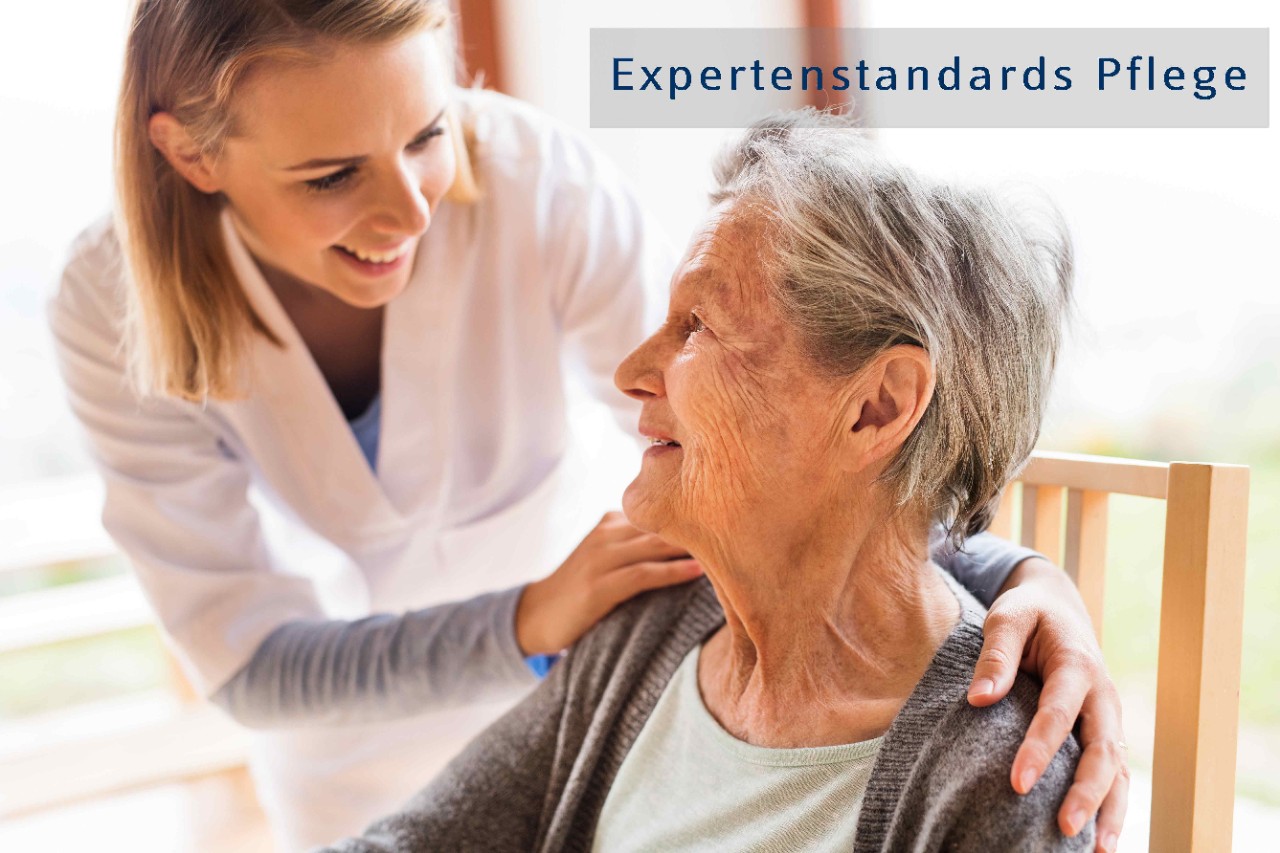 Pflegerin und Seniorin lächelnd beim Hausbesuch, Schriftzug: Expertenstandards Pflege