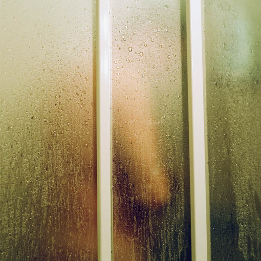 Blick durch eine Duschtür auf einen verschwommen sichtbaren Mann während der Dusche.